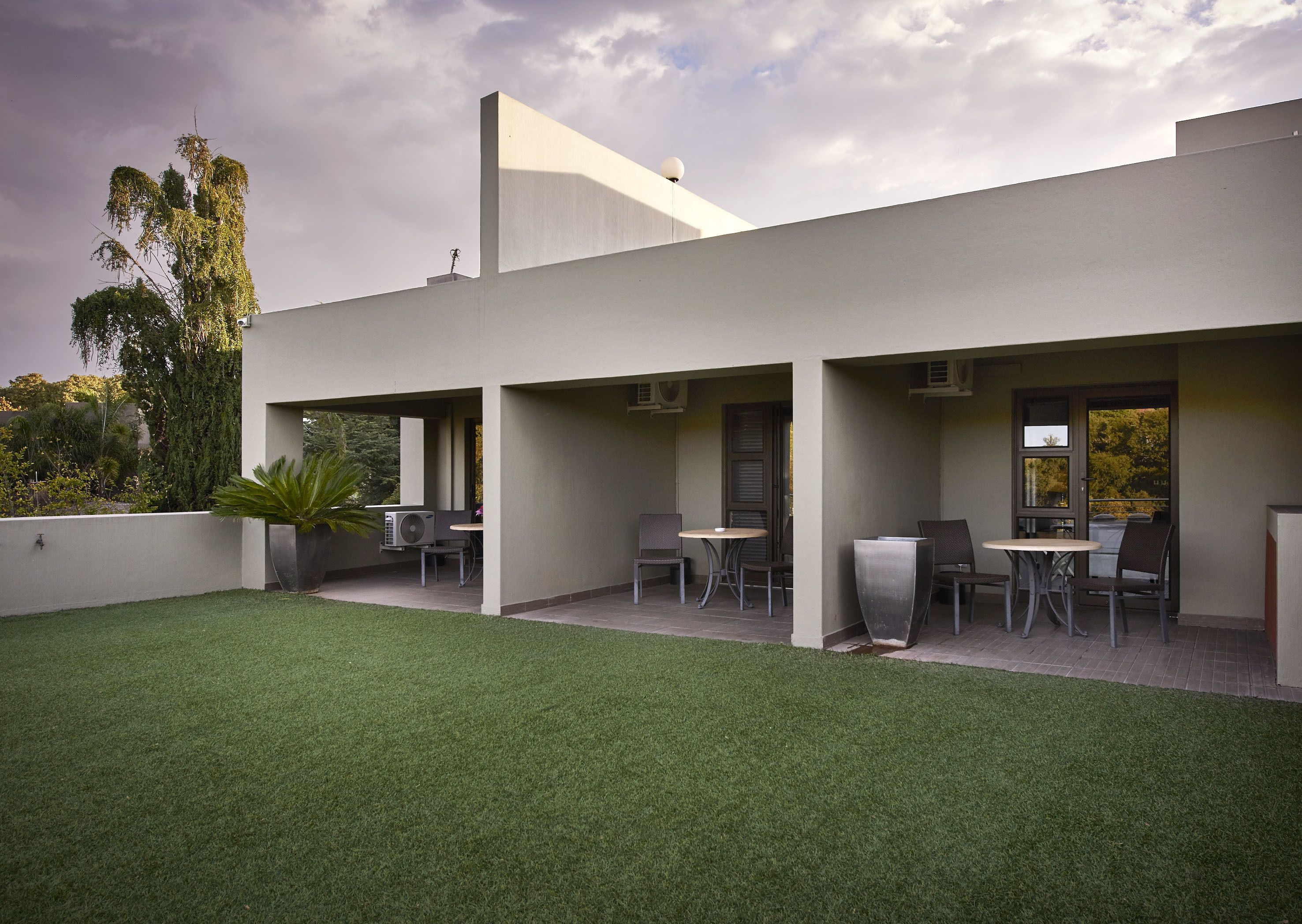 A modern building with a flat roof, outdoor seating area, and a well-maintained lawn.