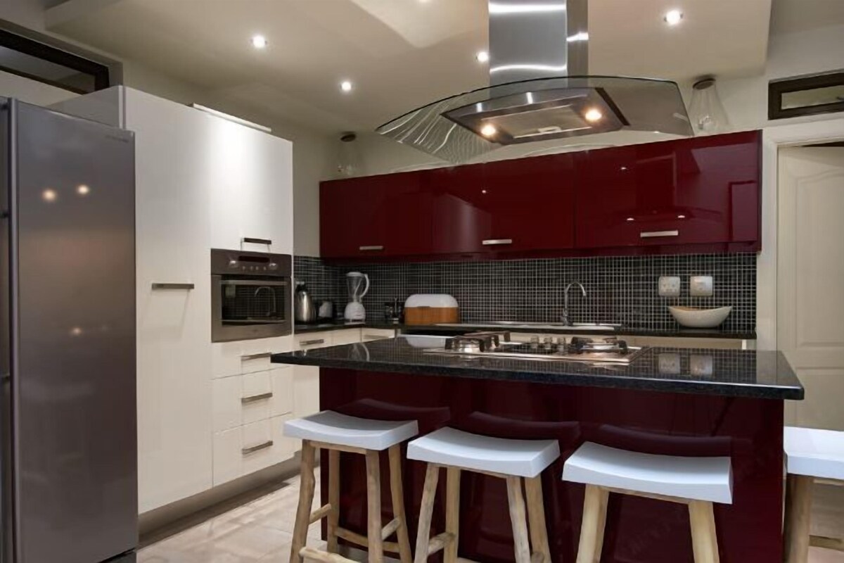Una cucina moderna con isola centrale, sgabelli da bar e frigorifero in acciaio inossidabile.