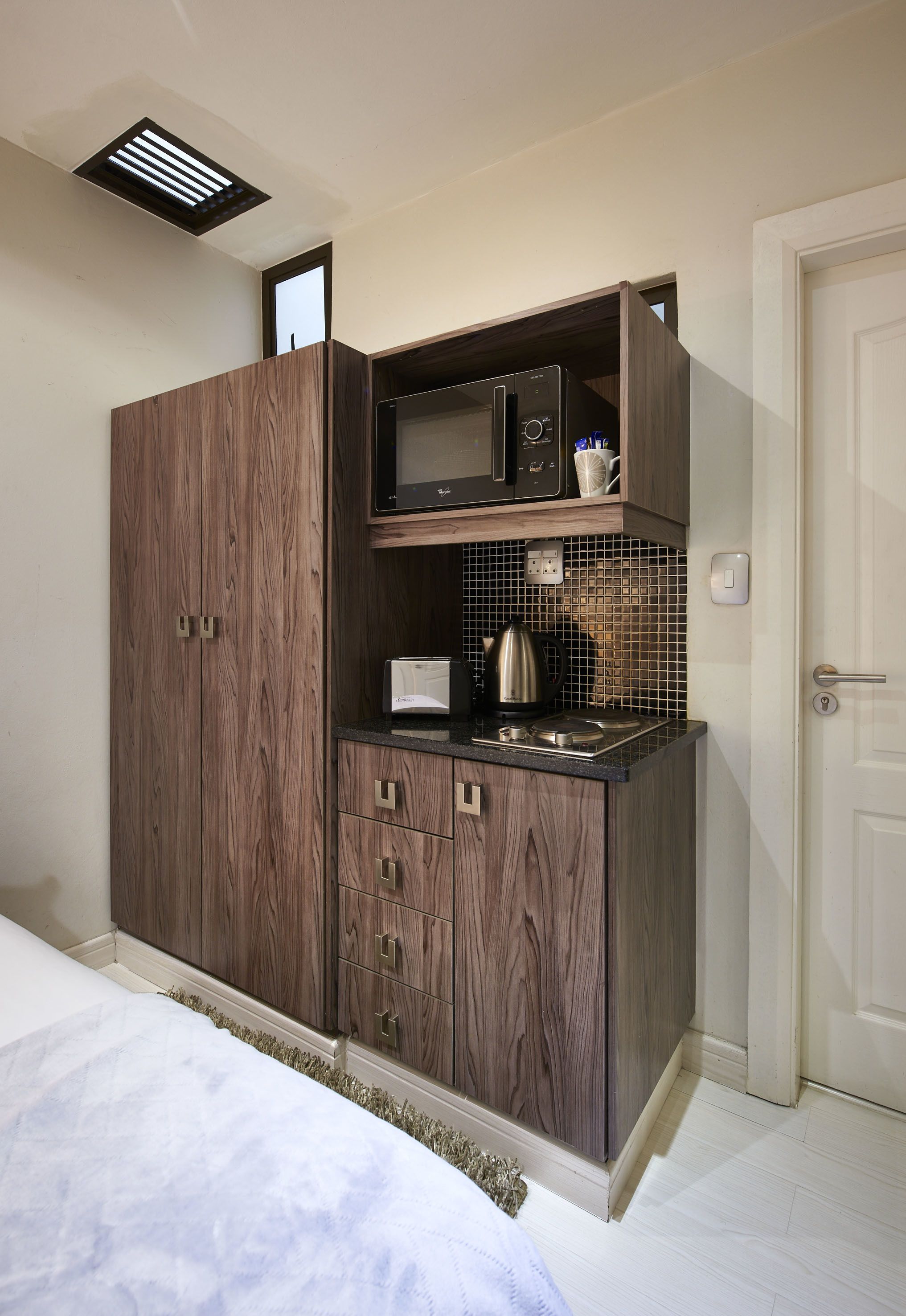 A compact kitchenette with a microwave, kettle, and small cabinet.