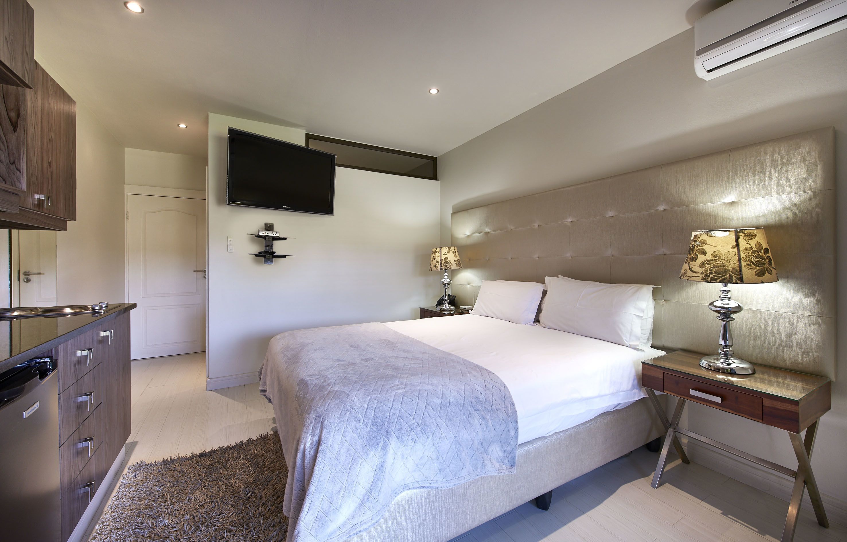A modern bedroom with a large bed, bedside tables, a flat-screen TV, and a wardrobe.