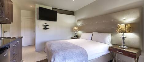 A modern bedroom with a large bed, bedside tables, a flat-screen TV, and a wardrobe.