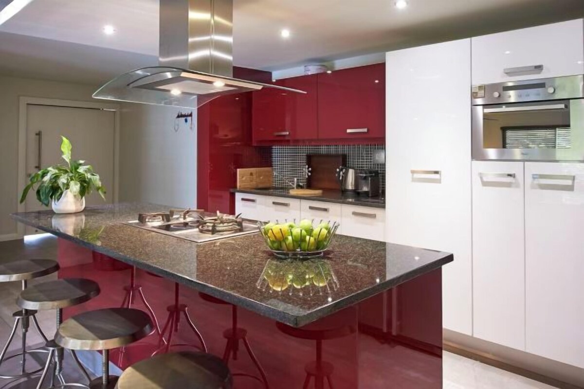 A modern kitchen with a central island, red cabinets, and stainless steel appliances.
