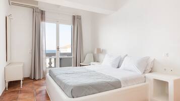 Habitación de hotel con una cama grande, un escritorio, una silla y vista al mar por la ventana.