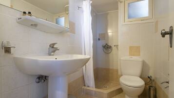 Baño con lavamanos, inodoro, ducha y una pequeña ventana.