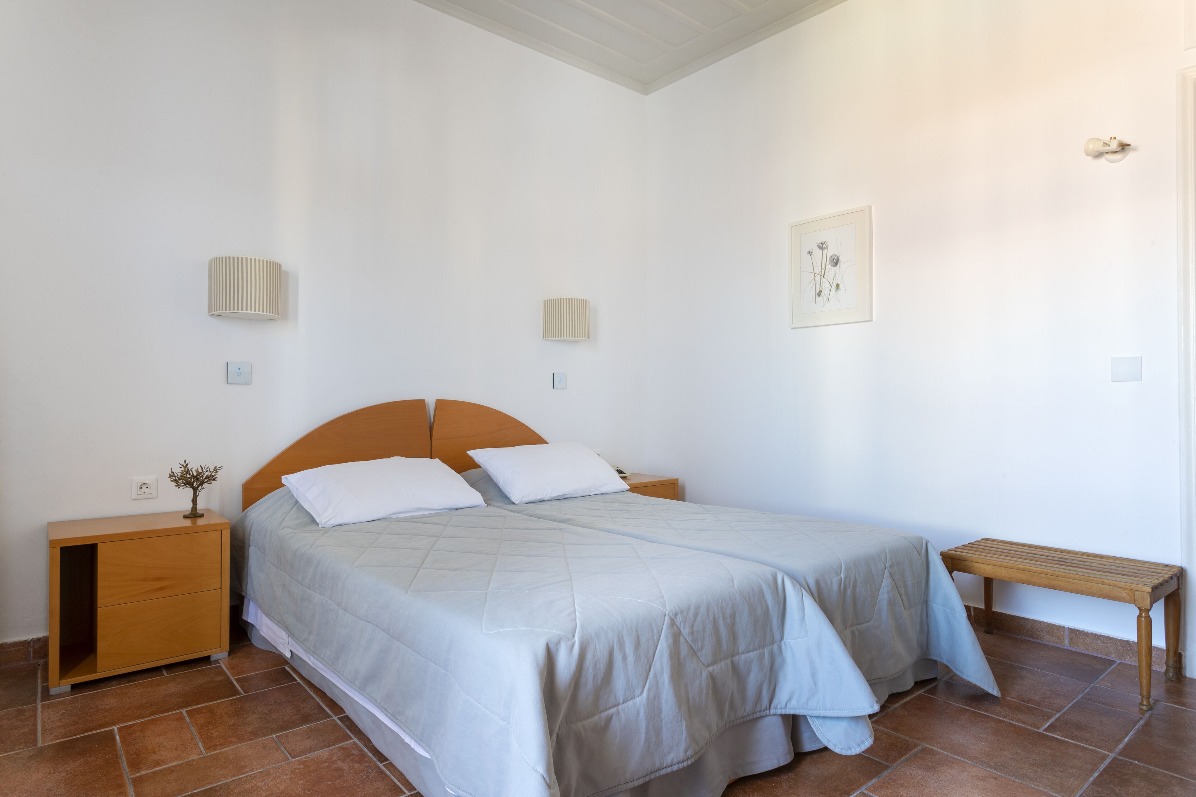 A bedroom with a bed, bedside tables, a bench, and wall-mounted lights.