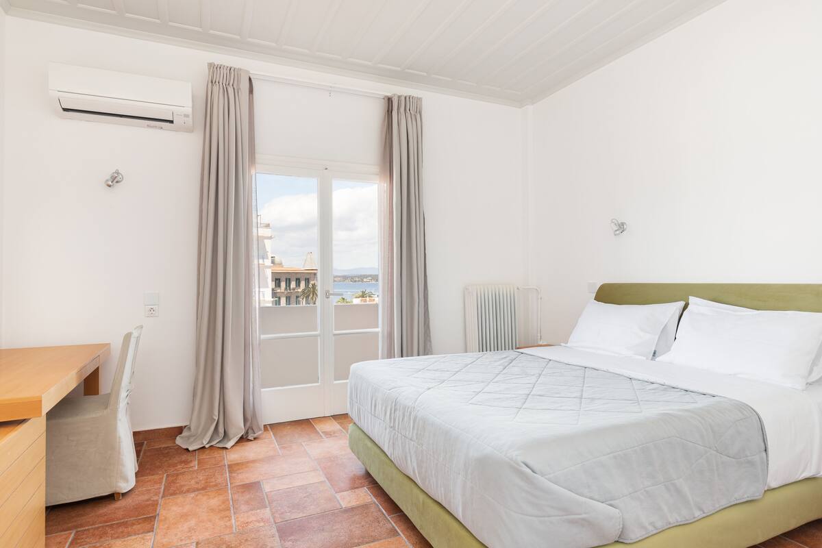 A bedroom with a bed, a desk, and a view of the outside.