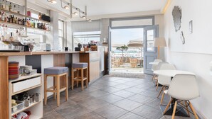 Zona de bar moderna con mostrador de madera, taburetes y vistas al área de mesas al aire libre.