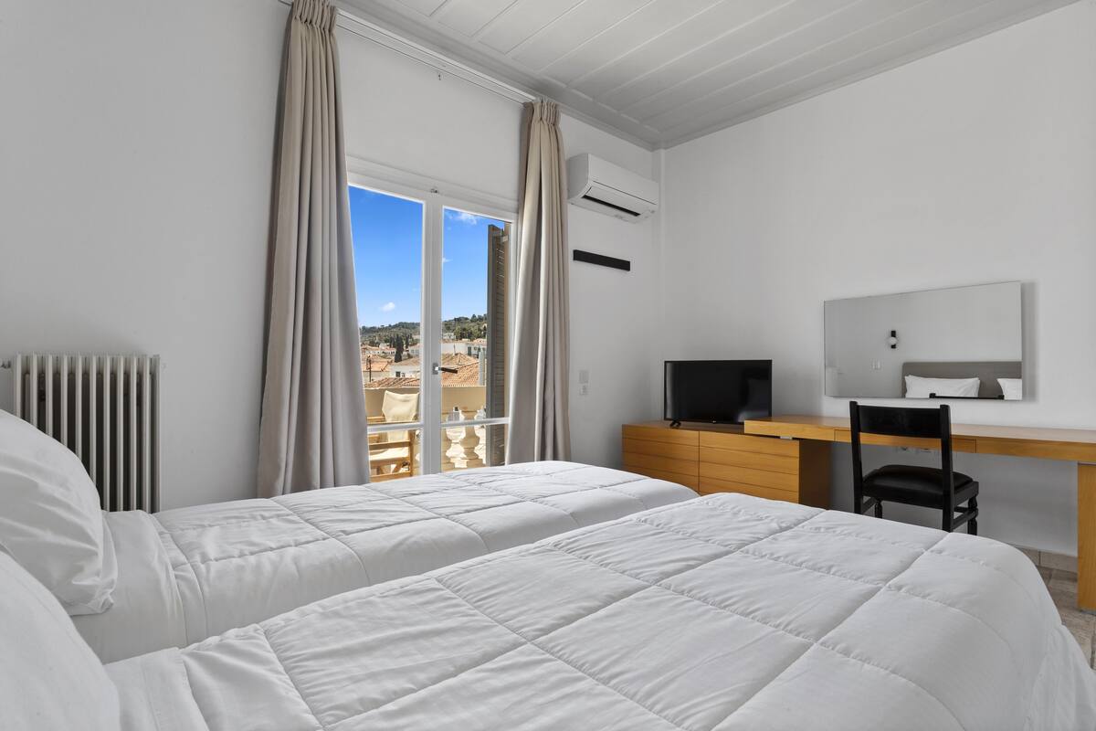 A bedroom with two beds, a desk, a chair, and a TV.