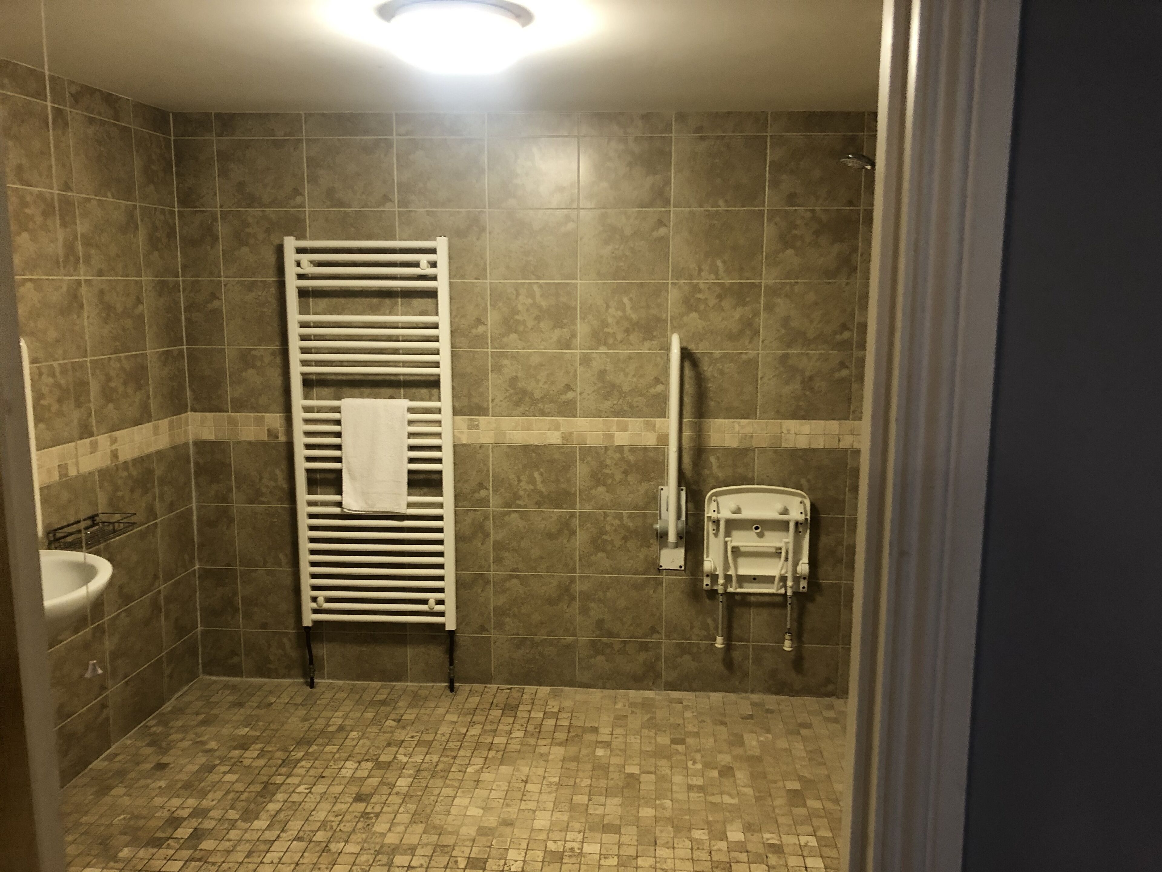 A bathroom with a tiled floor, a white sink, a towel rack, and a shower area.