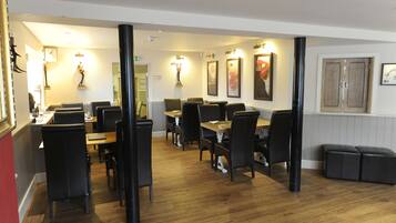 A restaurant with wooden tables and black chairs, framed artwork on the walls, and a wooden floor.