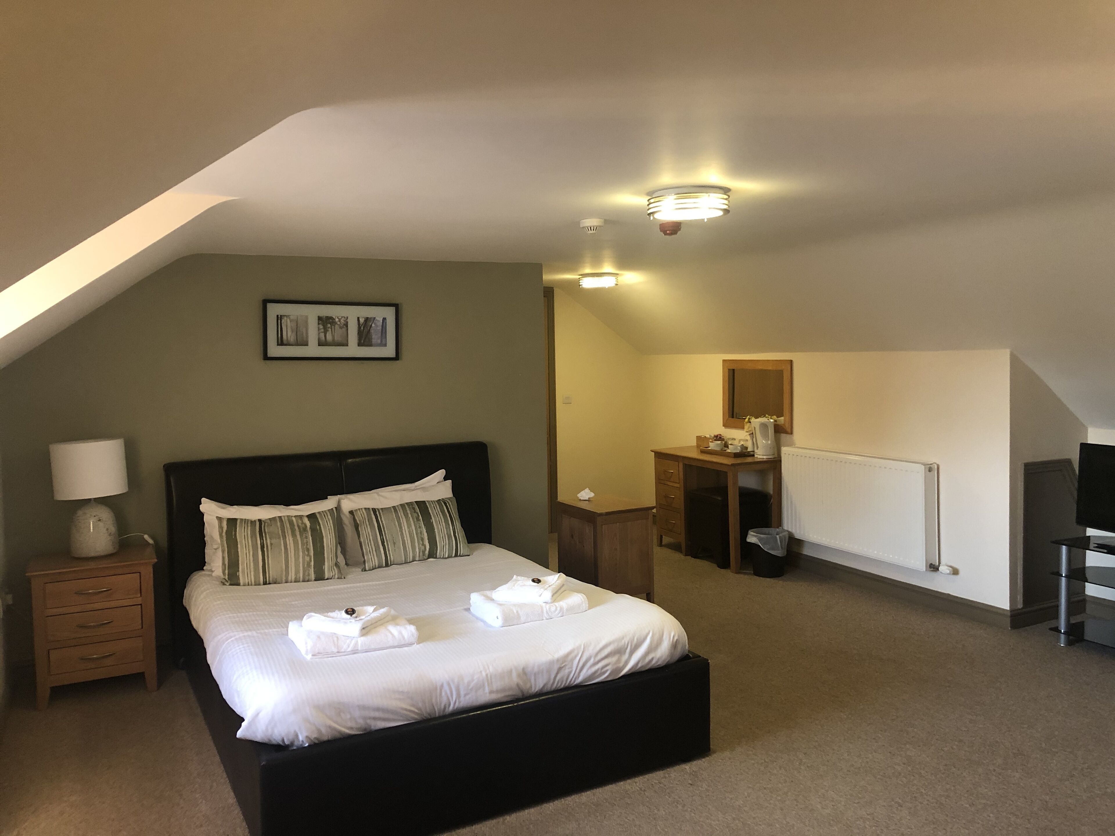 Ein Schlafzimmer mit Bett, Nachttisch, Lampe, Schreibtisch, Spiegel und Heizkörper.