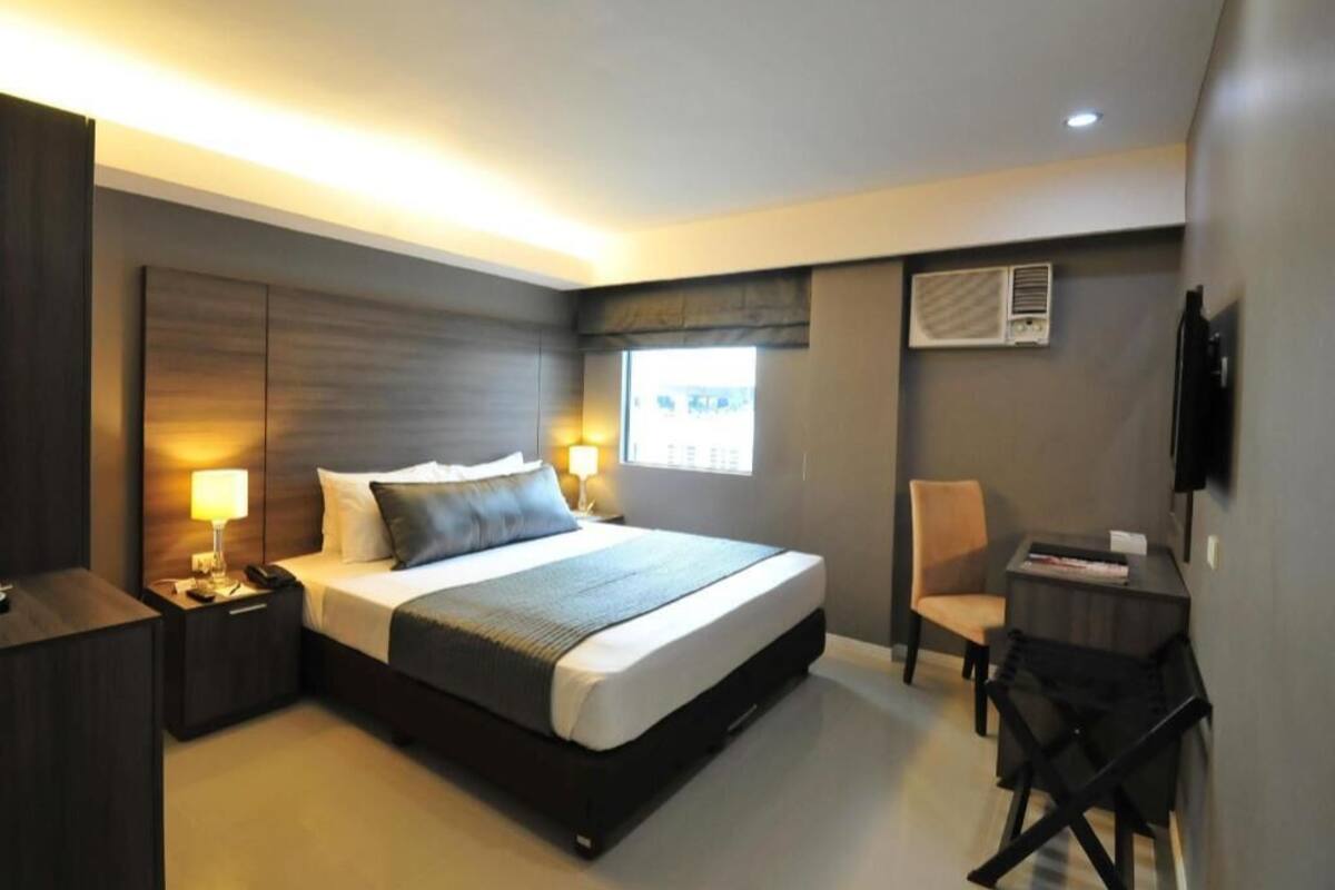 A modern hotel room with a large bed, bedside lamps, a desk, and a chair.