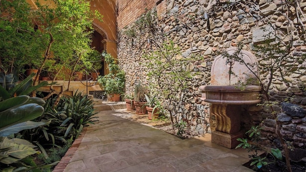 A stone pathway leading to a rustic building with a stone wall and potted plants.