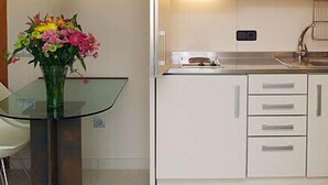 A compact kitchen with white cabinets, a glass table, and two white chairs.