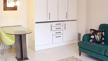 Un espacio habitable pequeño con una mesa de comedor, un sofá verde y un armario blanco.