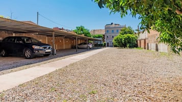 A parking area with gravel ground, covered parking structures, and a building in the background.