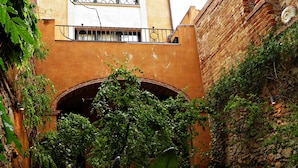 A courtyard with a brick wall, a balcony with a wrought iron railing, and potted plants.
