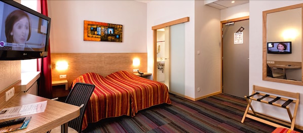 A hotel room with a bed, a desk, a chair, a TV, and a bathroom. - Hôtel Vendôme (Strasbourg)