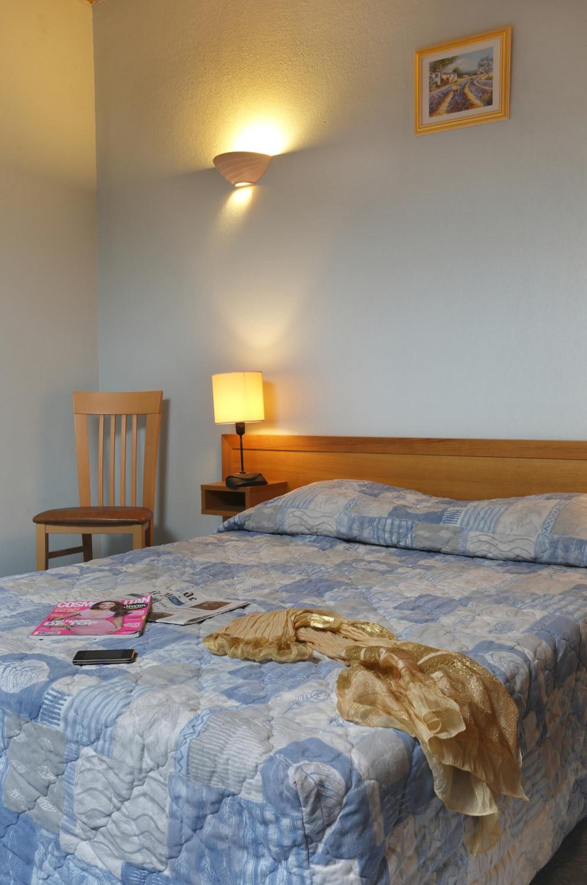 Ein Hotelzimmer mit einem Bett, einem Sessel, einem Nachttisch mit Lampe und einem gerahmten Bild an der Wand.