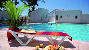 Ein Poolbereich mit Liegestühlen, einem Tisch mit Früchten und Getränken sowie einem klaren, blauen Pool.