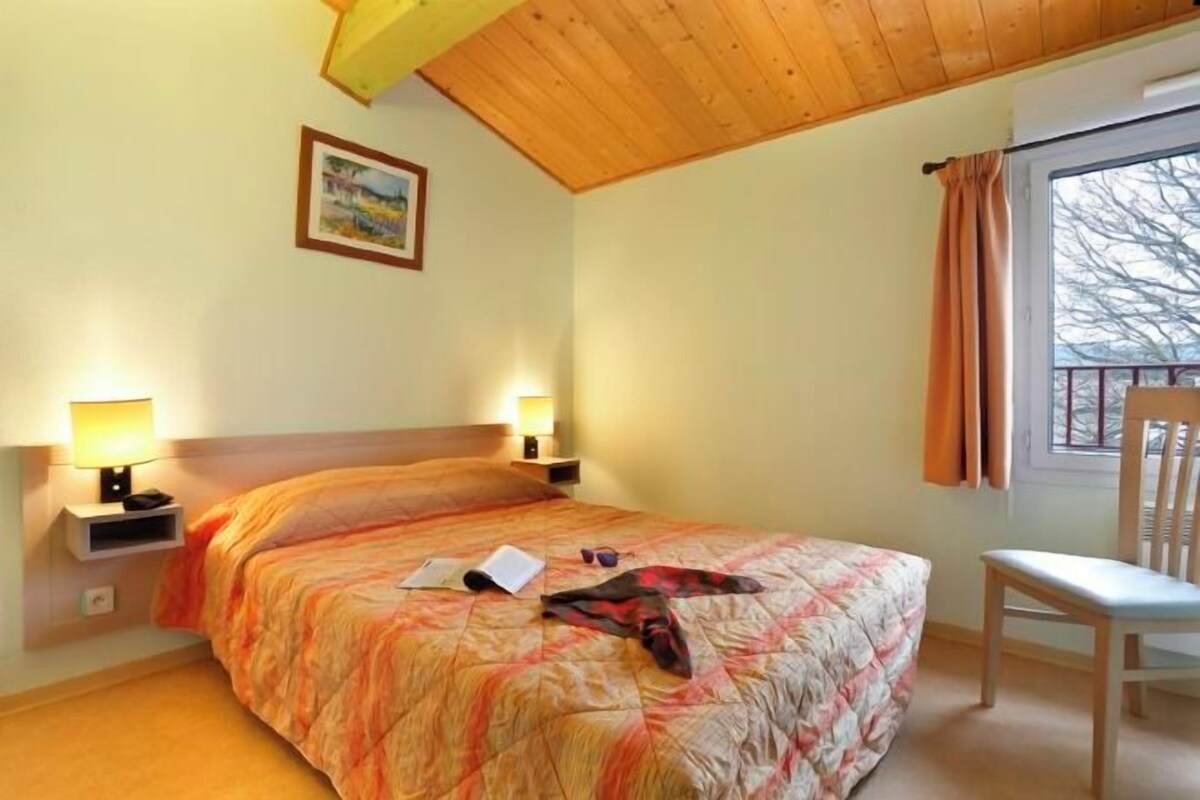 Une chambre d’hôtel avec un lit, deux lampes de chevet, une chaise, une fenêtre avec des rideaux et un tableau au mur.