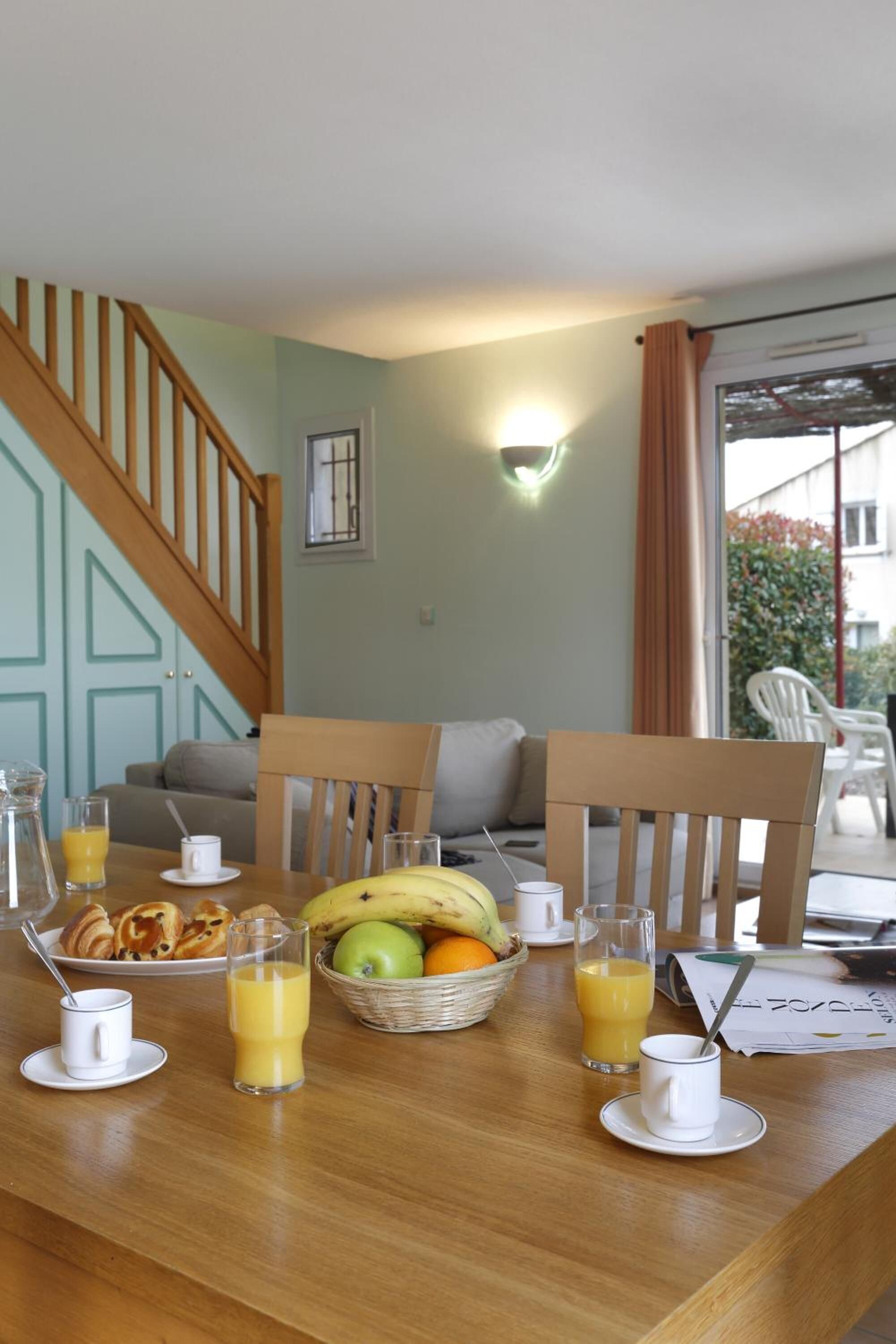 A breakfast table with croissants, bananas, apples, oranges, and juice glasses.