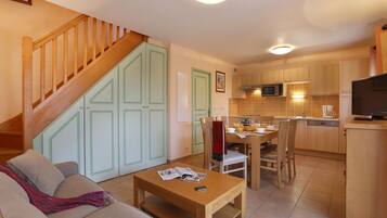 A modern kitchen with wooden cabinets, a dining area with a table and chairs, and a staircase leading to another level.