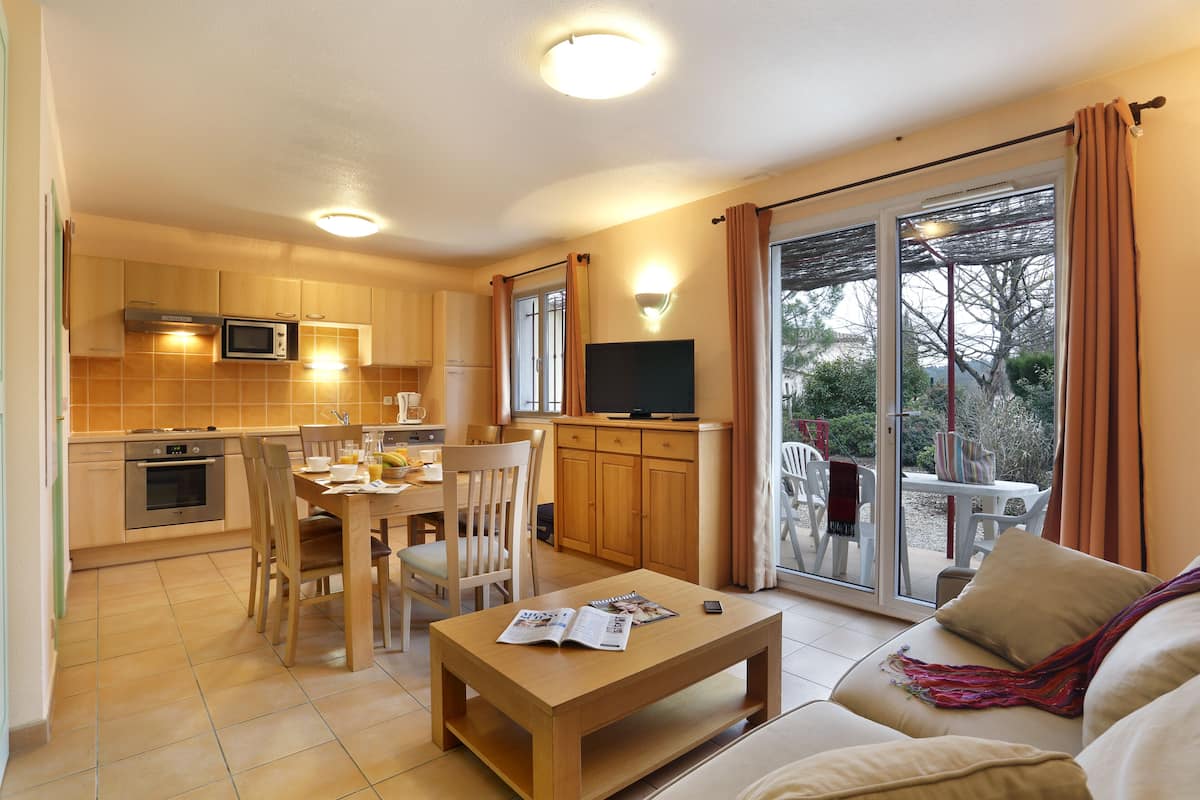 Une cuisine moderne avec des meubles en bois, une table à manger avec des chaises, une table basse avec un magazine et un canapé avec une couverture.