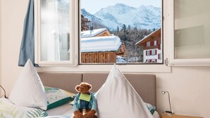 Ein Bett mit Teddybär, ein Fenster mit Bergblick und eine Holzhütte.