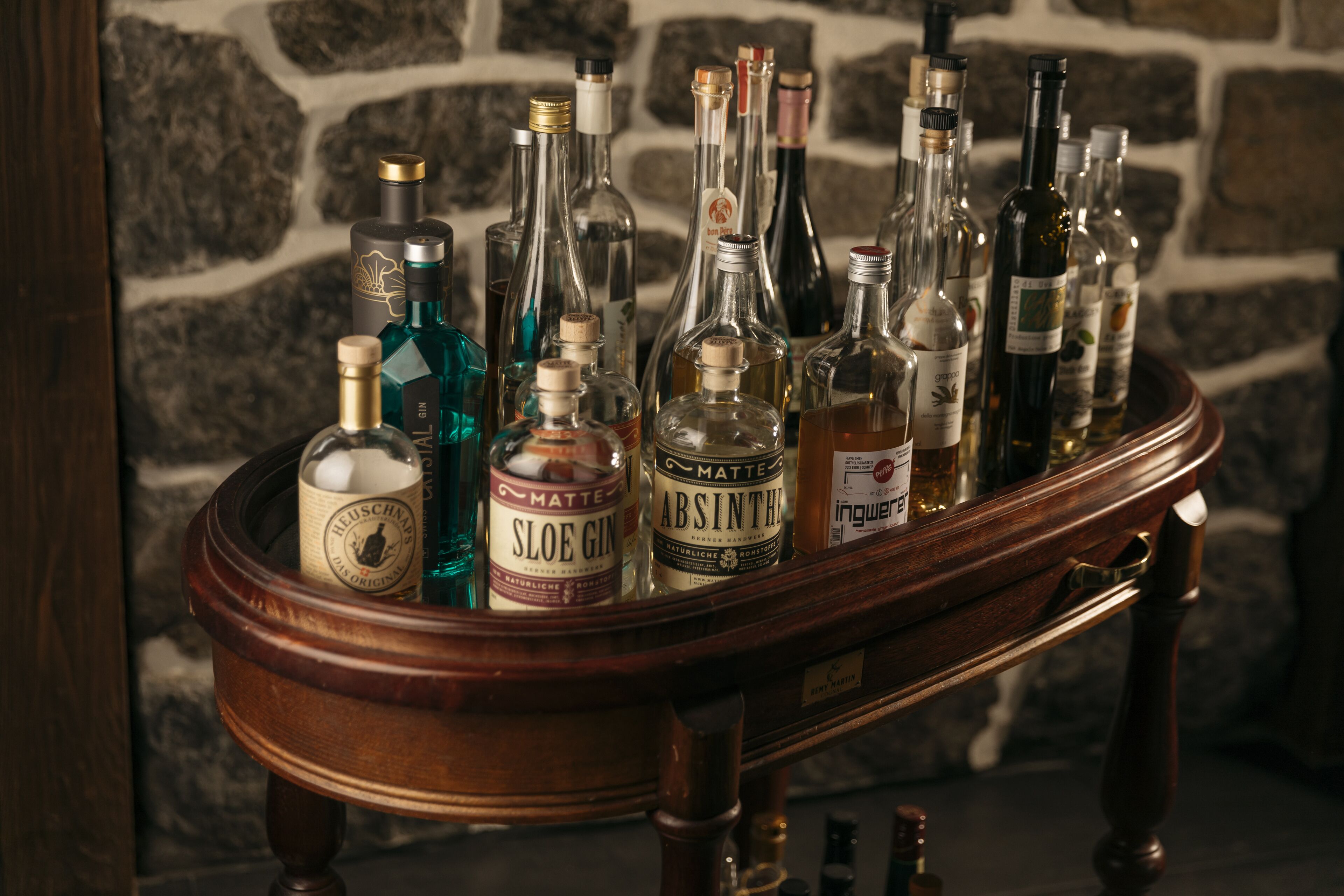 Eine Holztrennwand mit verschiedenen alkoholischen Getränken, darunter Gin und Absinth, vor einer Steinwand.