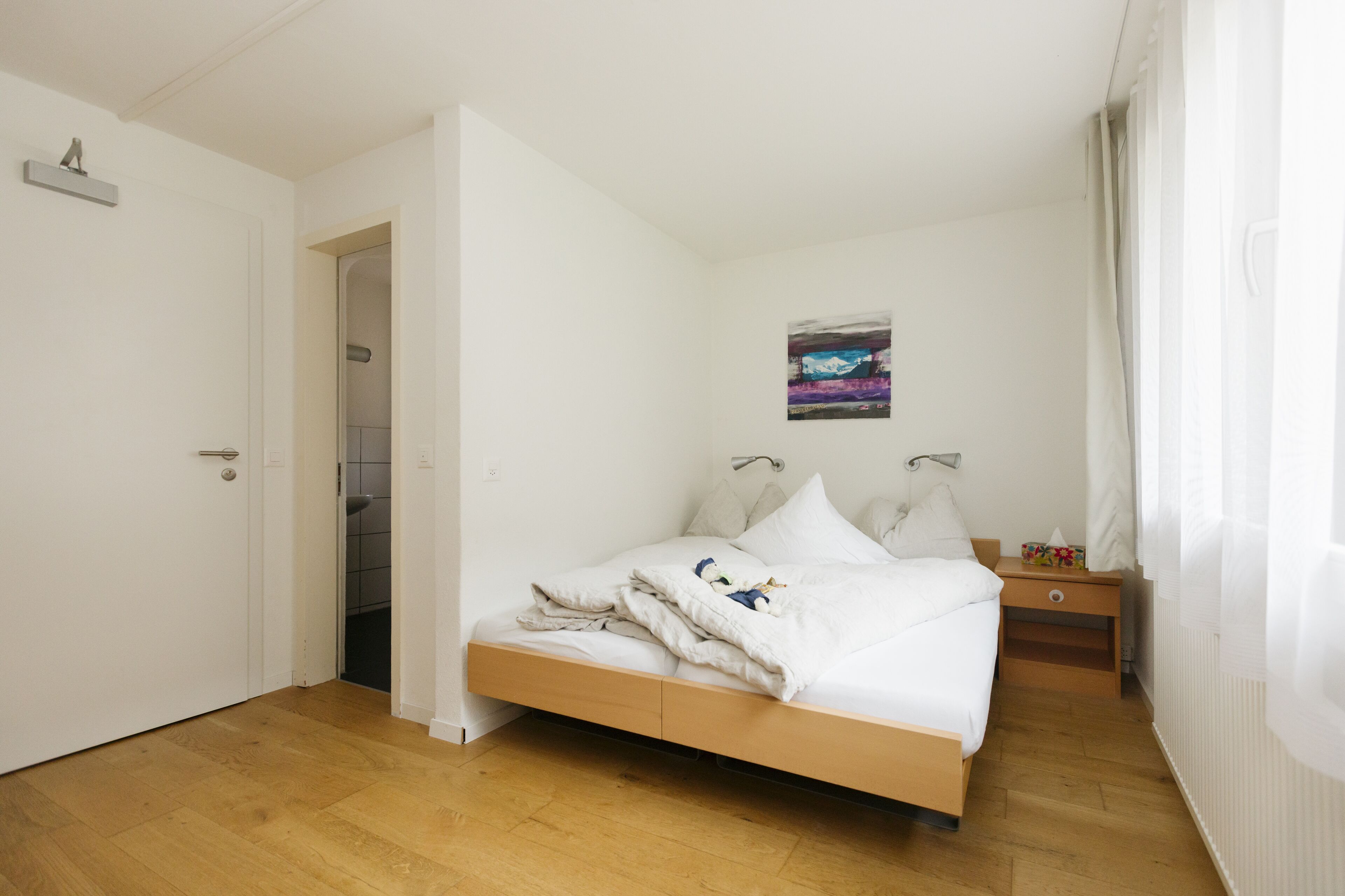 Une chambre à coucher avec un lit en bois, du linge de lit blanc, une table de chevet et un tableau accroché au mur.