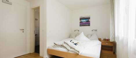 Une chambre à coucher avec un lit en bois, du linge de lit blanc, une table de chevet et un tableau accroché au mur.