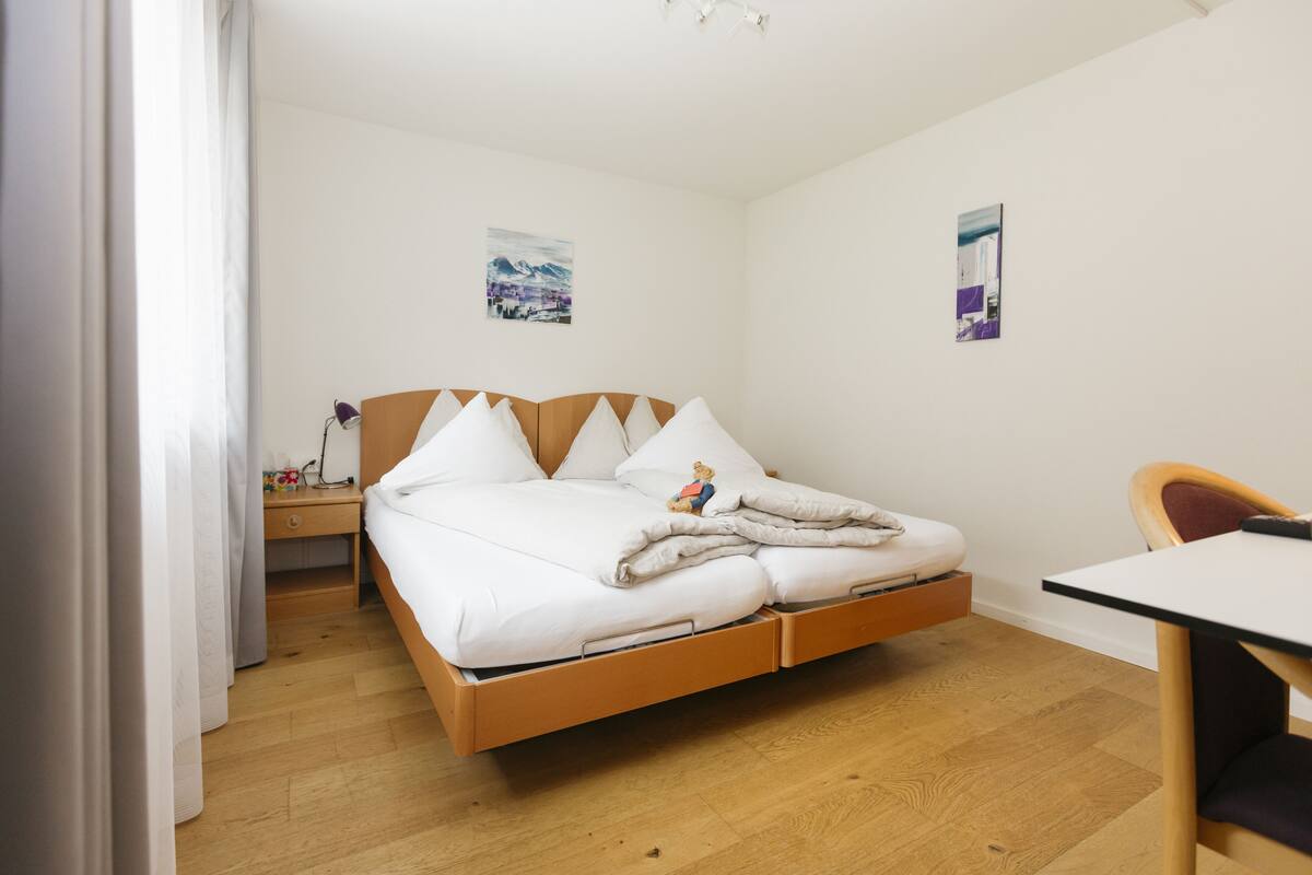 Une chambre à coucher avec un lit en bois, une literie blanche, une table de chevet avec une lampe et deux tableaux accrochés au mur.