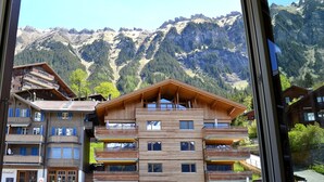 Ein mehrstöckiges Holzhaus mit Balkonen, vor einer Kulisse aus schneebedeckten Bergen und dichtem Wald.
