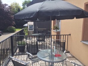A balcony with a glass table and chairs, a black umbrella, and a potted plant. - Platinium Hotel Aachen (Aachen)