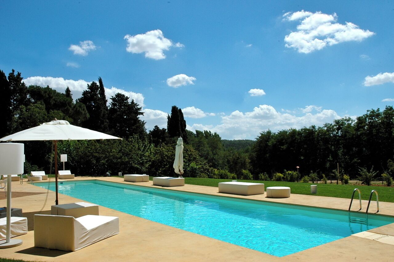 Una piscina rettangolare con acqua cristallina e azzurra, circondata da lettini e ombrelloni.