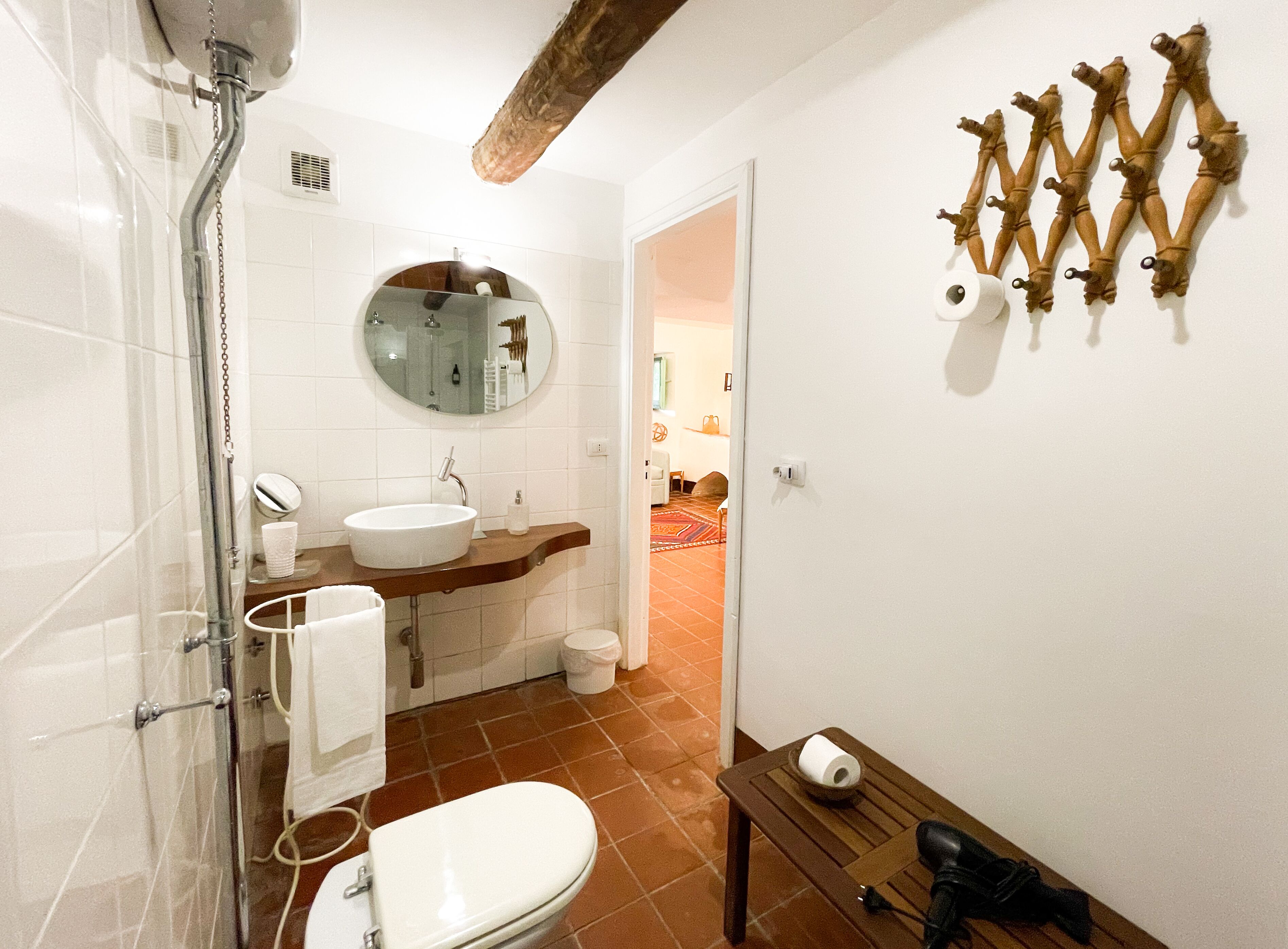 A bathroom with a shower, sink, toilet, and a wooden shelf with toiletries.