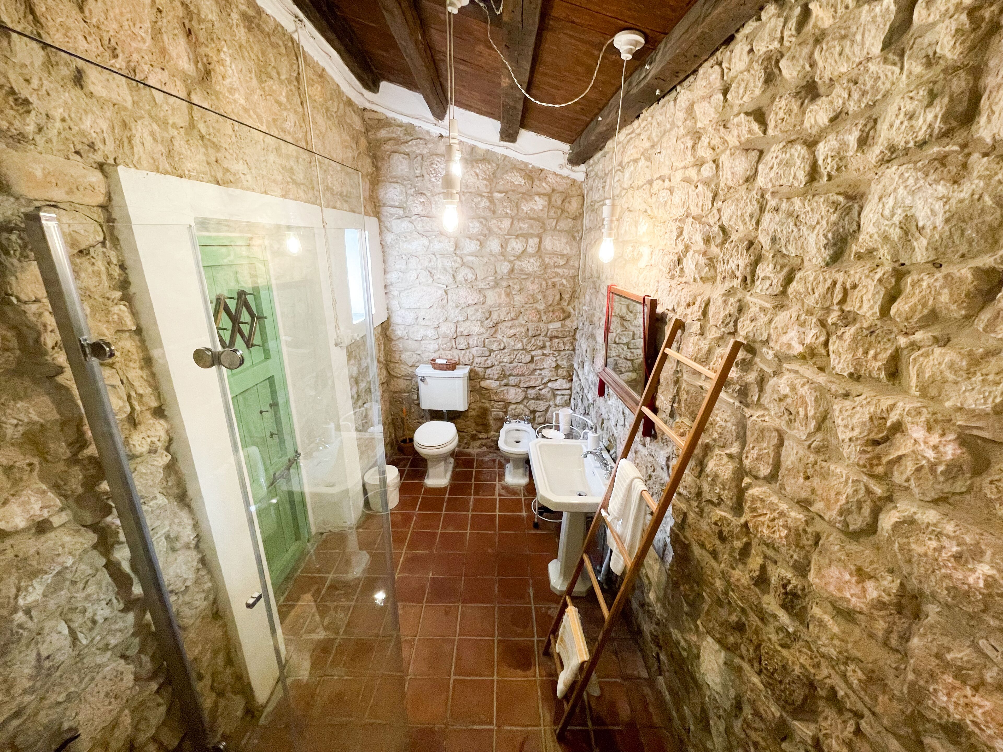 A stone-walled bathroom with a toilet, sink, and shower.