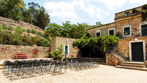 A courtyard with stone buildings, outdoor seating, and steps leading to a door. - Masseria Bannata (Enna)