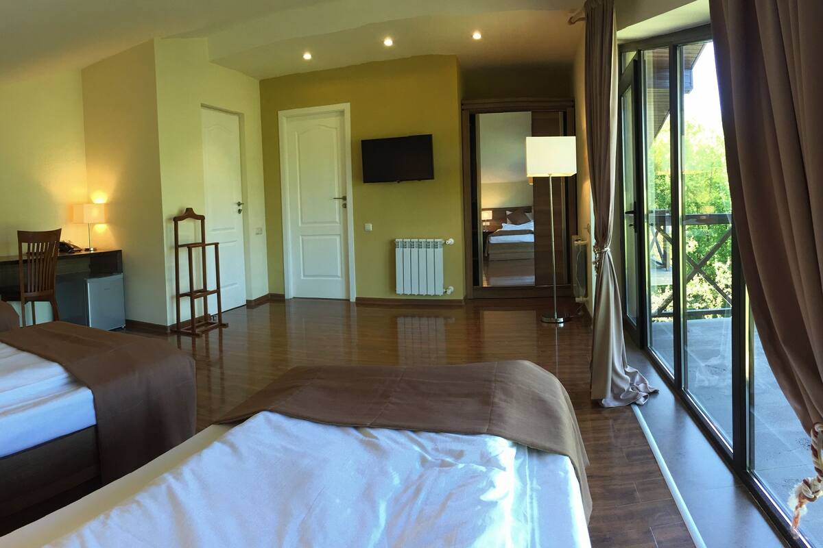 A hotel room with two beds, a desk, a chair, a television, and a balcony with a view.