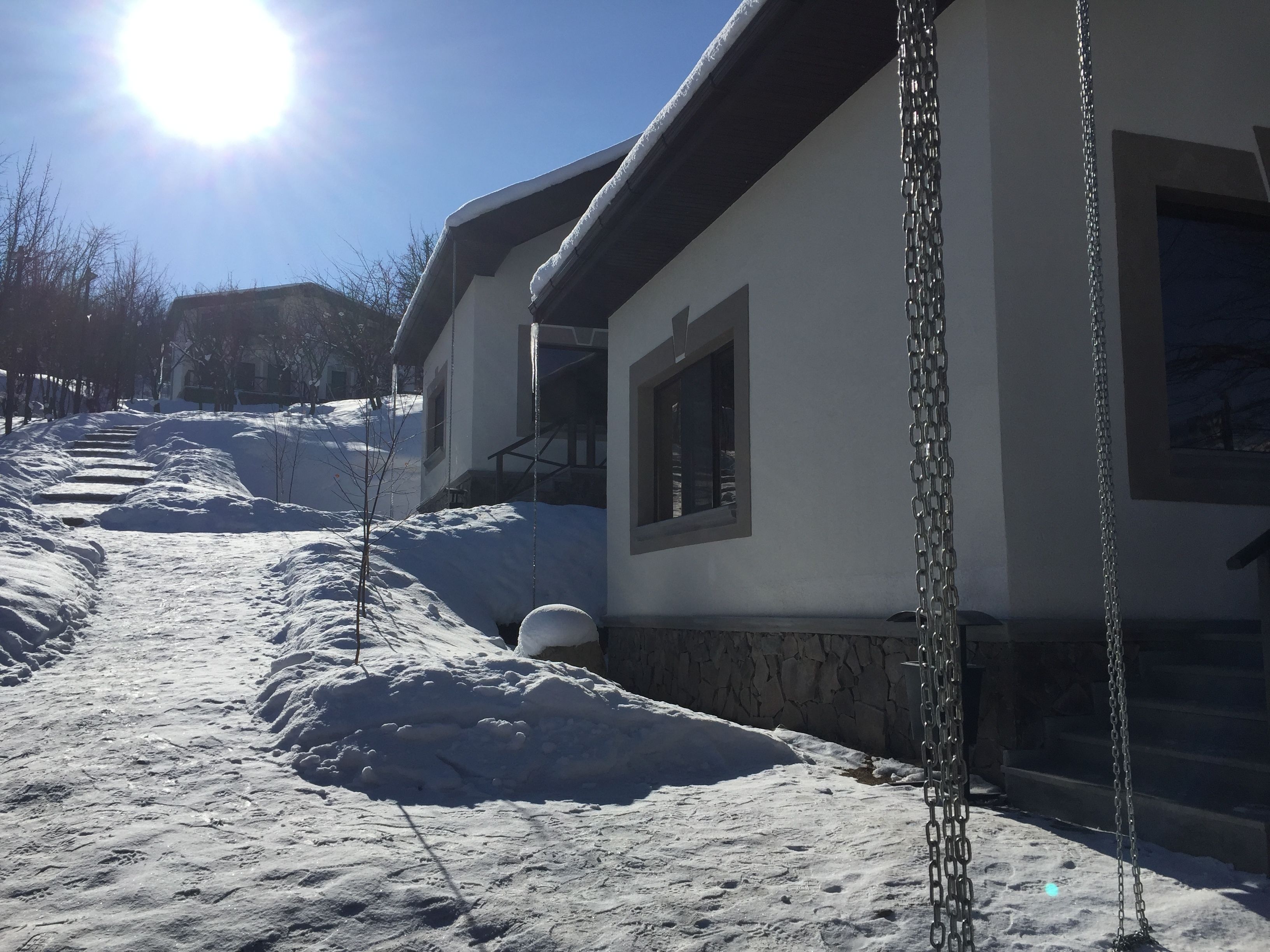 A snow-covered pathway leading to a house with a chain-link fence.