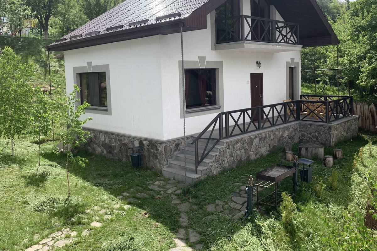 A two-story house with a stone foundation, a balcony, and a small outdoor seating area.
