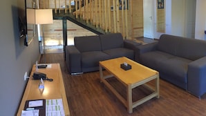 Een moderne woonkamer met een houten trap, grijze banken, een houten salontafel en een bureau met telefoon en documenten.