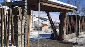 Een houten pergola met een metalen kettingzwaai, stenen muren en een besneeerd landschap op de achtergrond.