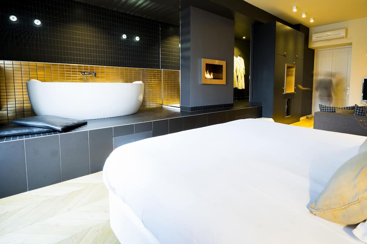 A modern hotel room with a large bed, a bathtub, and a separate shower area.