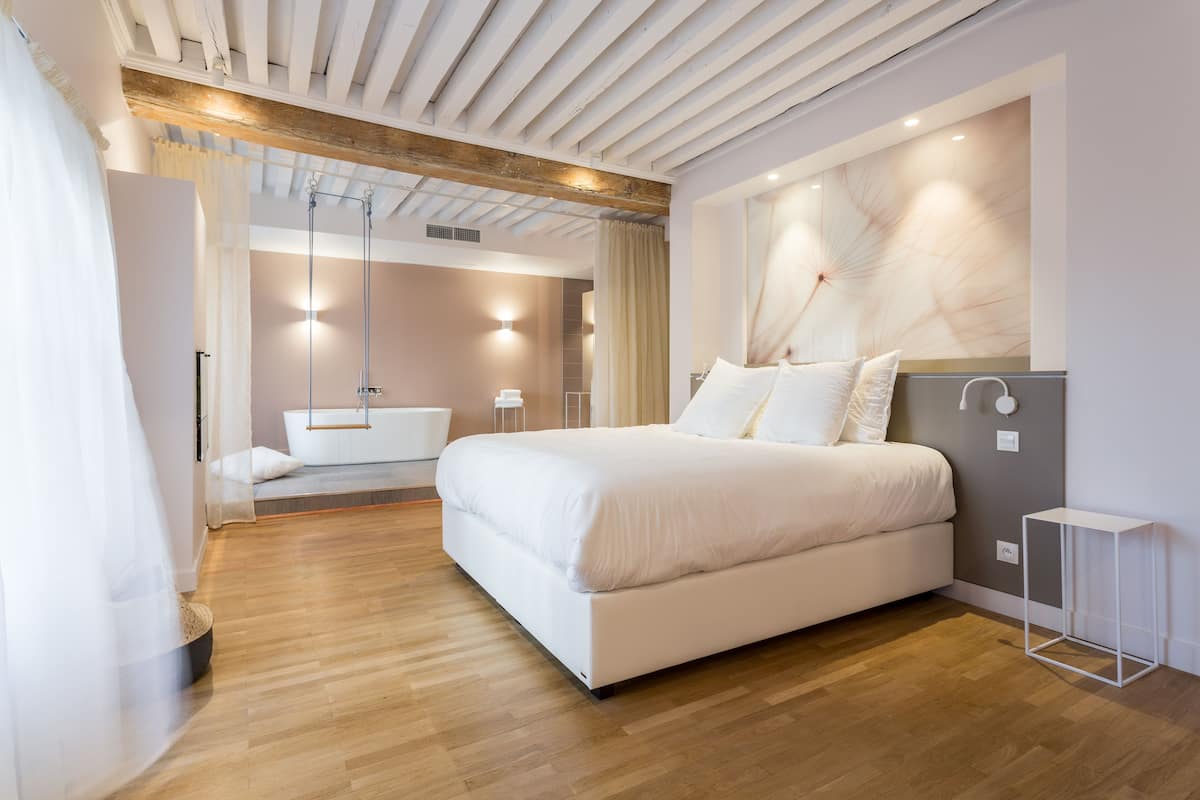 A modern bedroom with a large bed, a built-in bathtub, and a wooden ceiling.