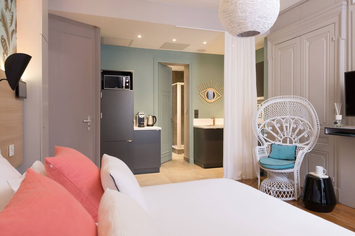 A bedroom with a bed, a white chair, a small table, and a television.