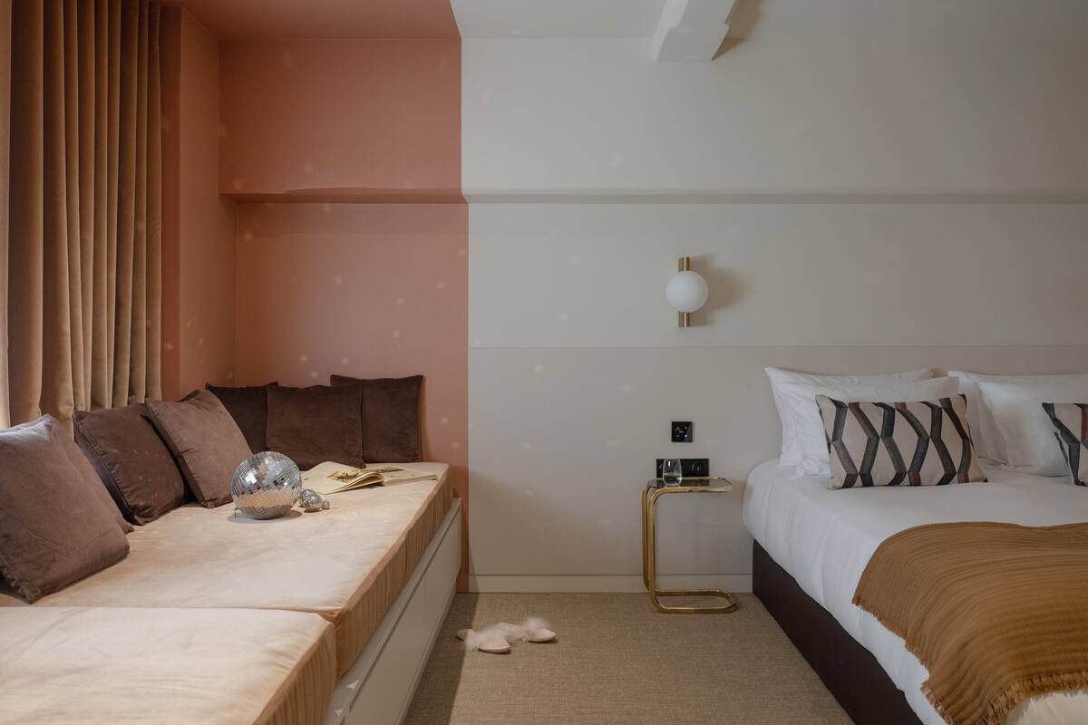 A bedroom with two beds, a bedside table, a lamp, and a window with curtains.