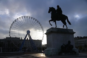A Ferris wheel and a statue of a man on a horse in an urban setting. - MiHotel (Lyon)
