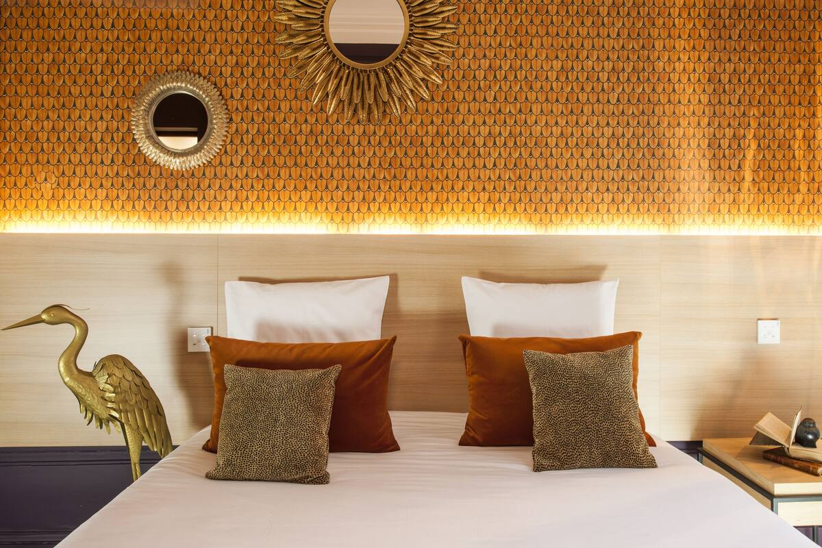 A hotel room with a patterned ceiling, a bed with white and brown pillows, and a decorative bird sculpture.